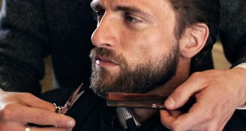 Here is man with a beard at the barber. The barber trim his beard with a beard trimmer